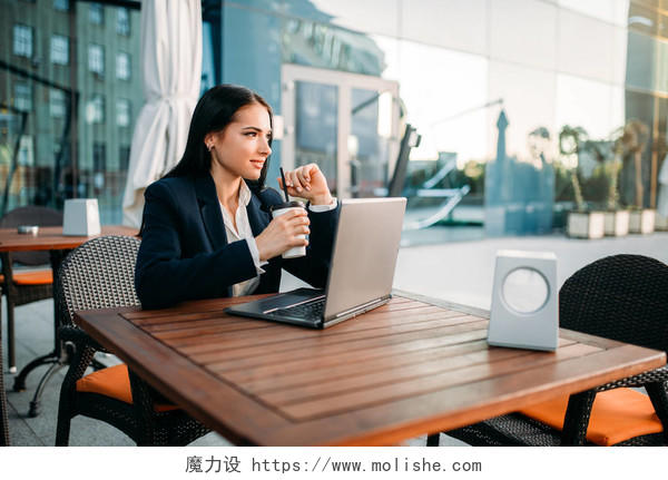年轻迷人的的快乐女实业家肖像工作与笔记本电脑和喝咖啡在街头咖啡馆
